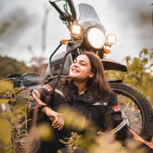Vishakha Fulsunge in a field, sitting in front of her motorcycle