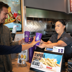 A restaurant worker handing reusable purple cups to customers