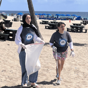Two people in Motorola t-shirts picking up trash on a beach