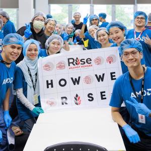 People in AMD t-shirts, gloves and hair nets posing for the camera with a sign that says: "How We Rise"