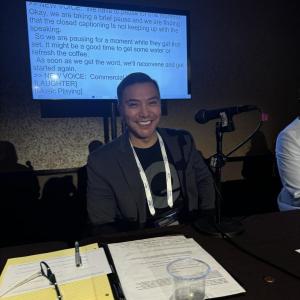 A person sat at a table in front of a projector screen 