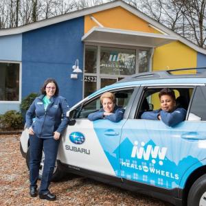 People in and around a stationary Meals on Wheels car