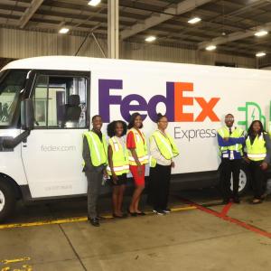 A group of people wearing hi-viz vests while stood next to a FedEx express van