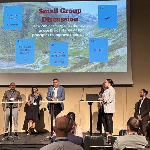 People on a stage underneath a screen that says Small Group Discussion