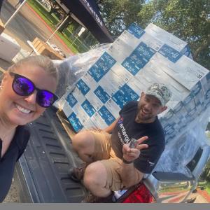 People smiling next to new fans in boxes placed in the bed of a pickup truck