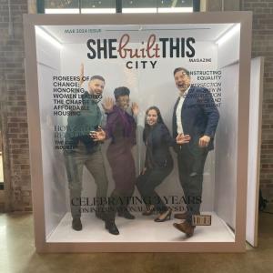Four people posing inside a glass box decorated as if on a magazine cover