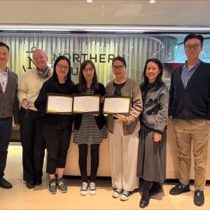 7 people standing in an office together, 3 holding diplomas