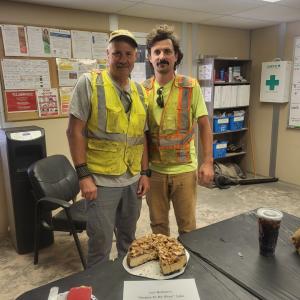 Two people in high-visibility vests standing together behind a table with a cake on it