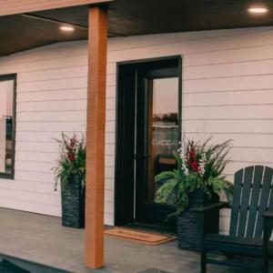 Exterior of the 3D printed home's front porch. Two chairs and a table to the side, plants on the sides of the doorway.