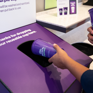 Someone dropping a reusable purple cup into a bin