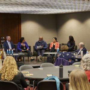 An audience of people watching and listening to a group of speakers 