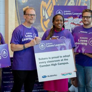 A group of people wearing purple t-shirts and holding Subaru loves learning boxes