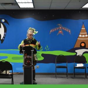 Someone speaking at a podium, with a large mural in the background