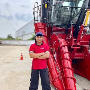 A person stood with their arms folded next agricultural machinery 