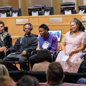 Four young people seated and facing a seated audience, two holding microphones