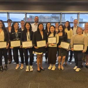 A group of people standing together, those in the front holding diplomas