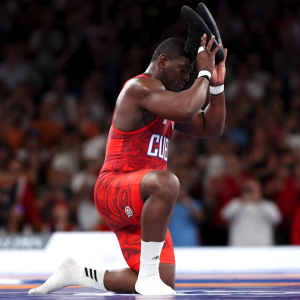 An Olympian on a mat holding shoes above their head