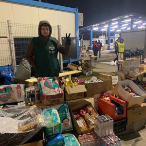aide worker standing behind a row of boxes of supplies like diapers, water, soaps.