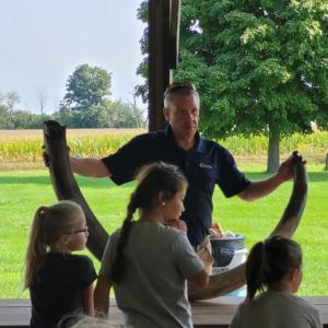 An adult holding a large tusk on a picnic bench as kids watch on.