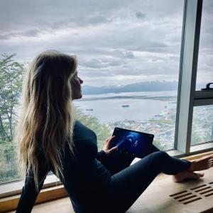 Gádor leaning back on a bench in front of a large window while viewing an image on a tablet