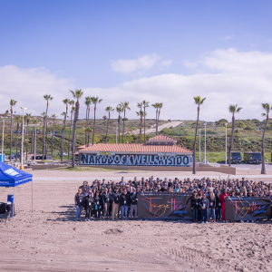 People standing in a group outside, with palm trees and sky in the background