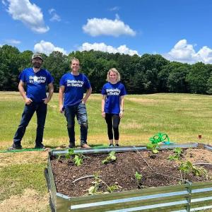 Three people stood behind a raised bed in a field for planting fruit and veg