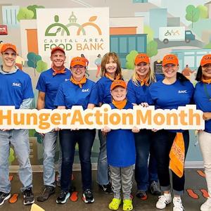 A group of volunteers wearing blue t-shirts and orange caps, holding a 'hunger action month' sign