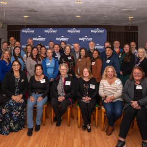 A smiling group of people posed for the camera, six seated in front and the rest standing behind them