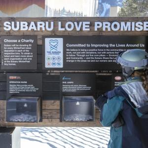 A person in a ski helmet reading a board that says "Subaru Love Promise"