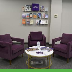 Three empty chairs, a table with pamphlets, and a collection of pamphlets on a wall in the background