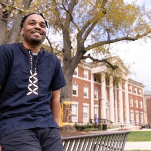 Dr. LeNiles leaning on a bench in front of a tree
