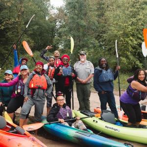 People on shore standing next to colorful kayaks and holding up paddles