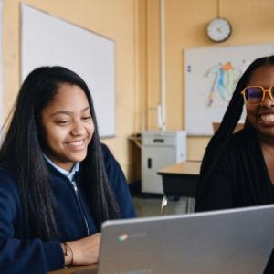 Two people sat at a table next to each other working on a laptop