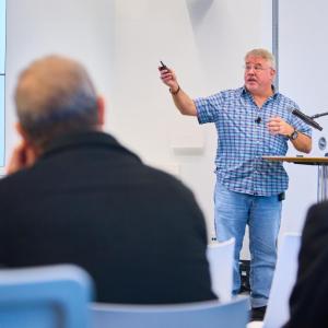 Man on stage points at presentation on "Green Chemistry" to an audience. 