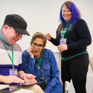 Three adults smiling while looking at a tablet.