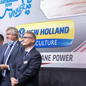 3 peple stand with an Award in front of a sign that reads: New Holland Culture