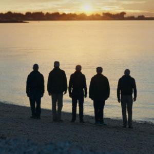 Five people stood on a beach watching the sunset 