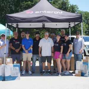 People standing together outside under an Entergy tent, with boxes of new fans