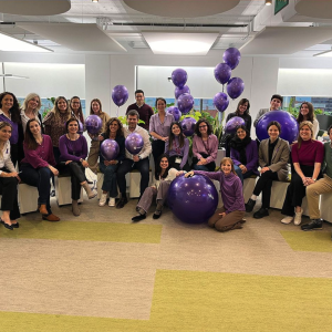 A group of people inside with purple balloons and a purple yoga ball