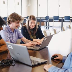 Four people at a conference table working on laptops