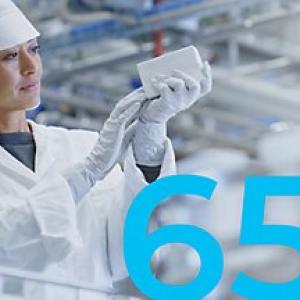 A person in protective garments looking at a white object. "65%" on the right.