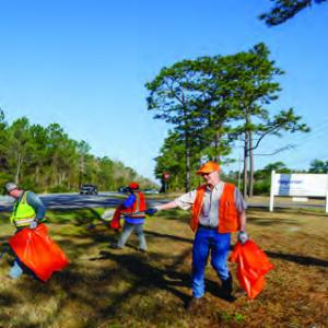 Three people working together outside to clean a grassy area