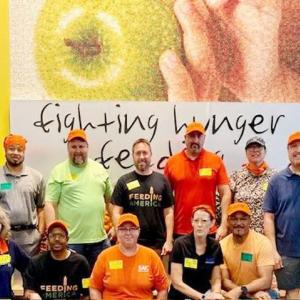 A group of people stood in front of a sign that reads 'fighting hunger feeding'