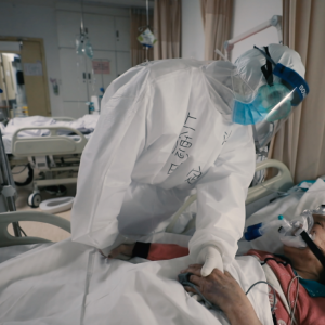 person in full PPE holding hands with a patient in bed