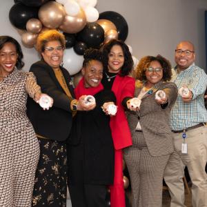 A line of smiling people posed, each holding out a round object.