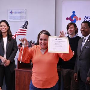 A program participant holds up a certificate of achievement and a small American flag during a ceremony at the Arab-American Family Support Center.