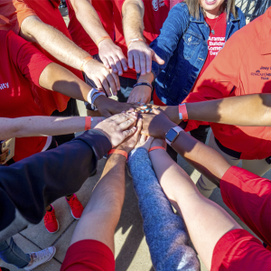 Aramark volunteers join their hands together in the center of a circle as part of a team huddle