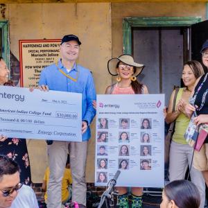 A small group, some holding a large check, and another holding a board with images of scholarship recipients.