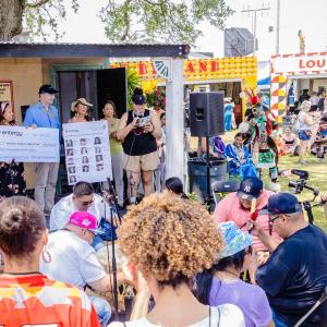 A small group, some holding a large check, and another holding a board with images of scholarship recipients in front of a small crowd.