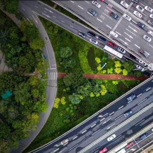 Aerial view of intersecting highways and traffic. An area of trees and grass are central and to the left side.
